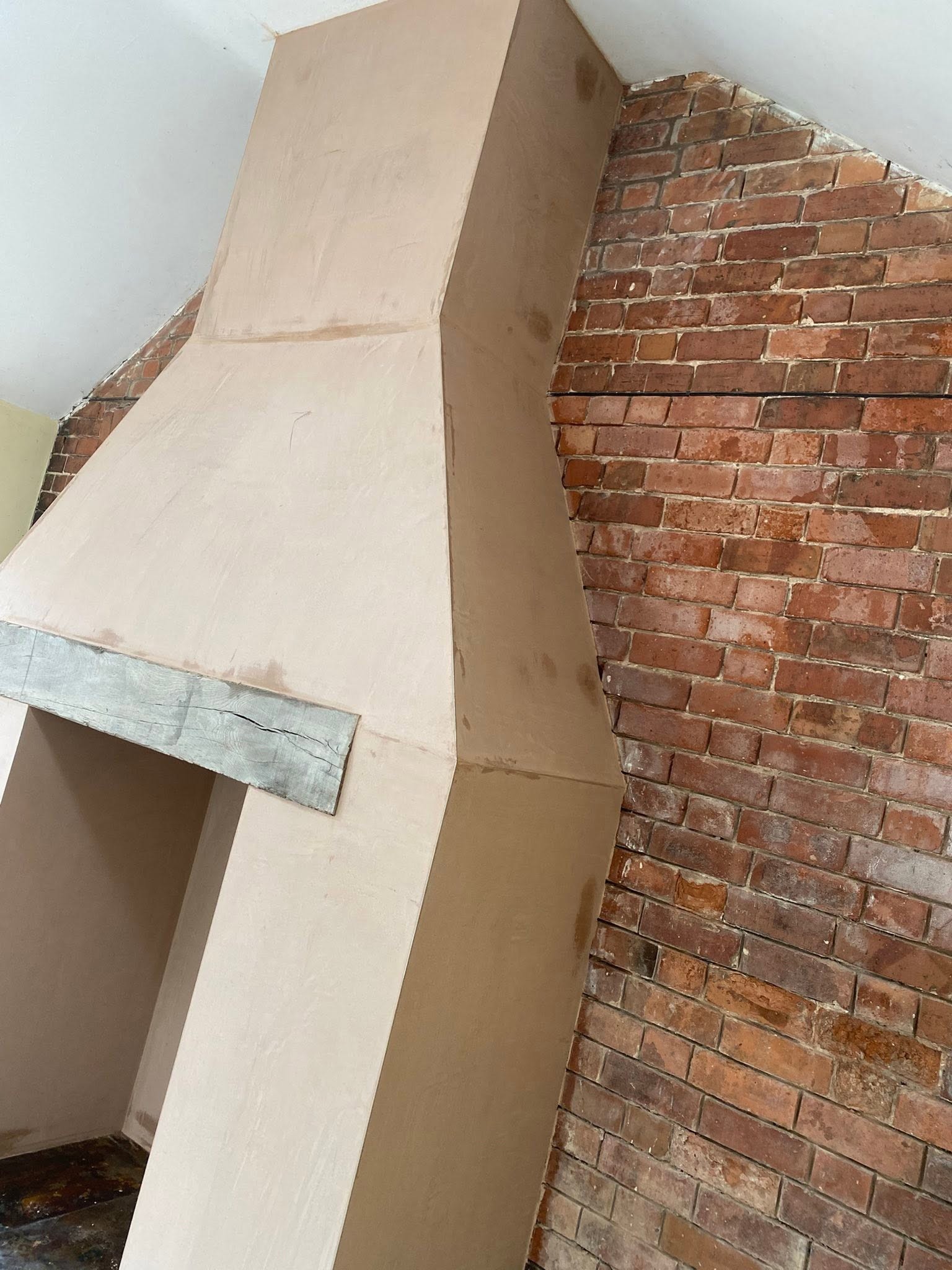 Close view of the plastered fireplace surround and oak beam beside old brick in Ruyton-XI-Towns